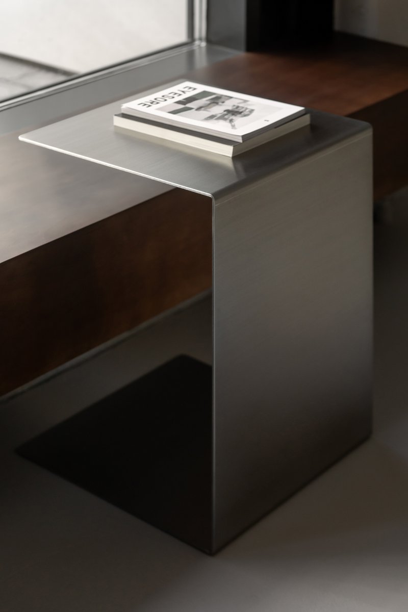 Close-up of brushed stainless steel side table with a book resting on its cantilevered top