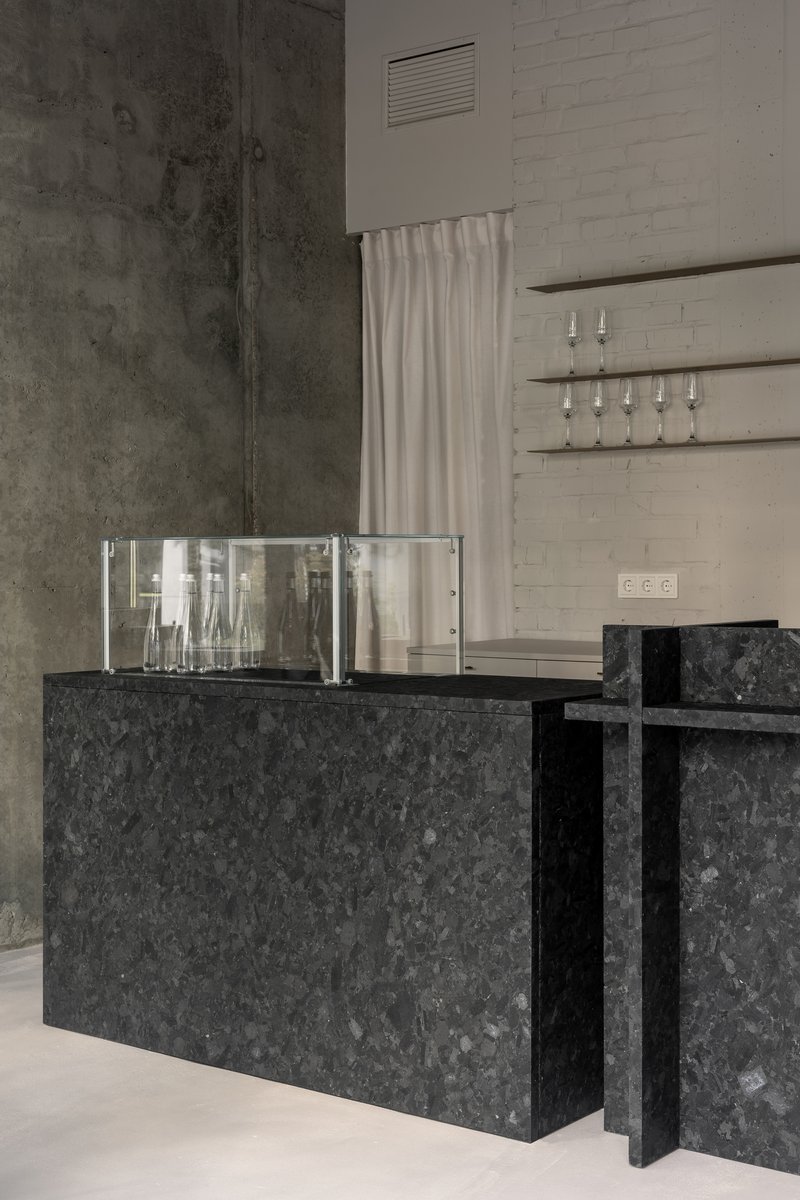 Reception counter in dark speckled stone with glass display box and concrete walls behind white curtain