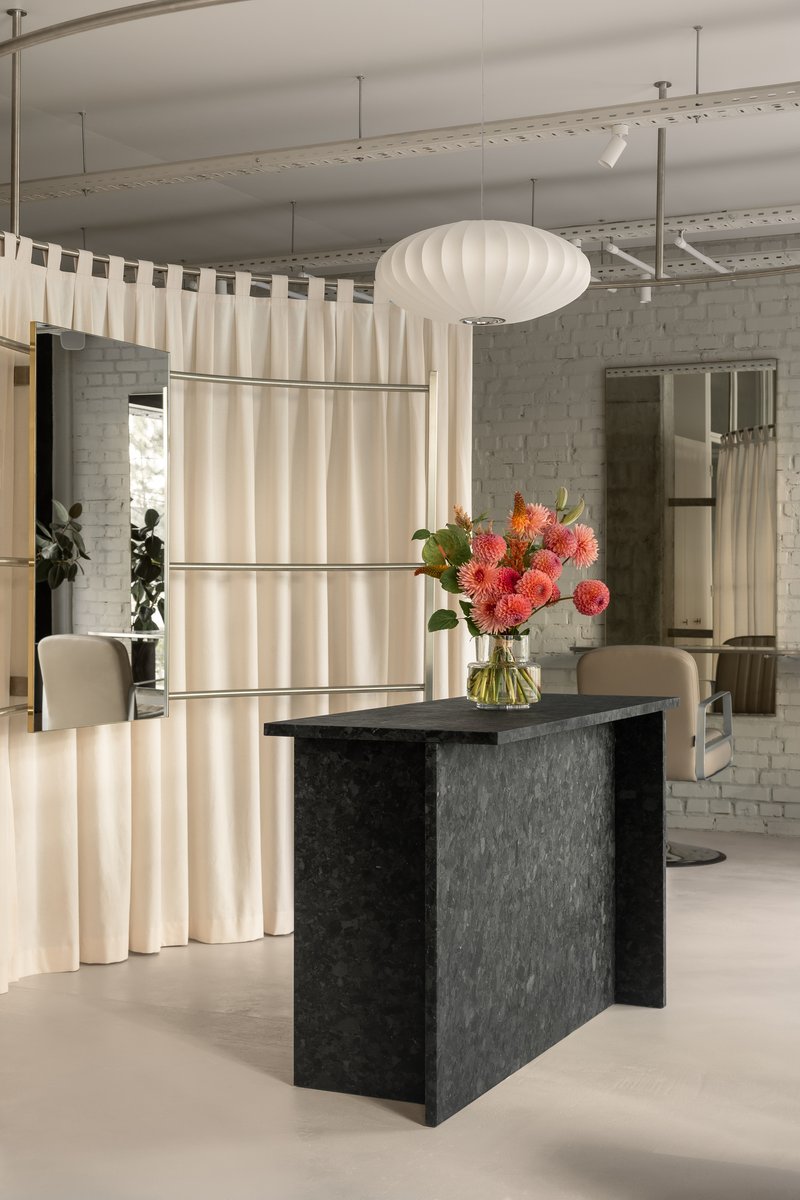 Reception area with dark stone table holding coral flowers beneath pleated pendant light and curtain screens