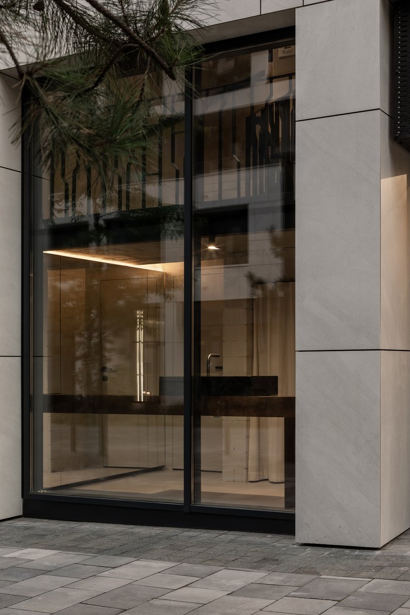 Street view through glazed storefront with black frames showing illuminated interior counter at dusk