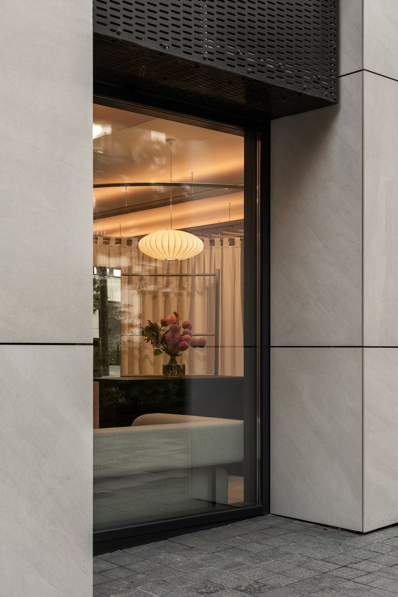 Corner window at twilight revealing interior with pleated pendant lamp and flowers reflected in glass