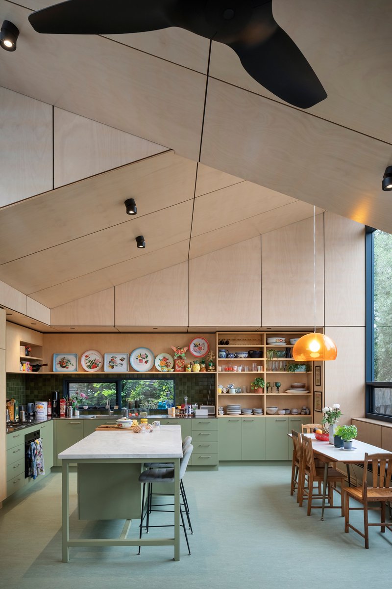 Open-plan kitchen and dining area with plywood ceiling panels and green cabinetry below open shelving