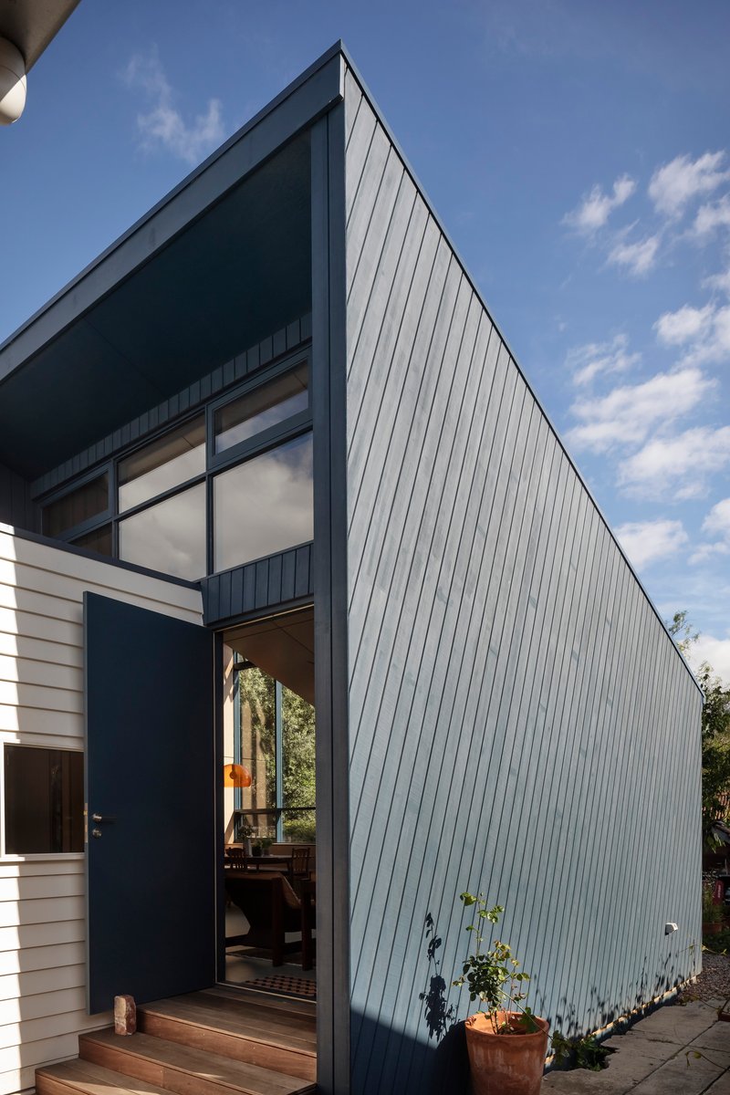 Gabled volume clad in vertical metal panels with recessed entry and potted plants at the threshold