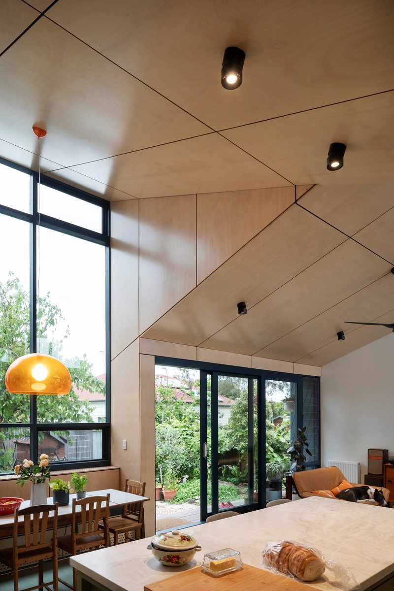 Interior view of angled plywood ceiling with black downlights and kitchen island in afternoon light