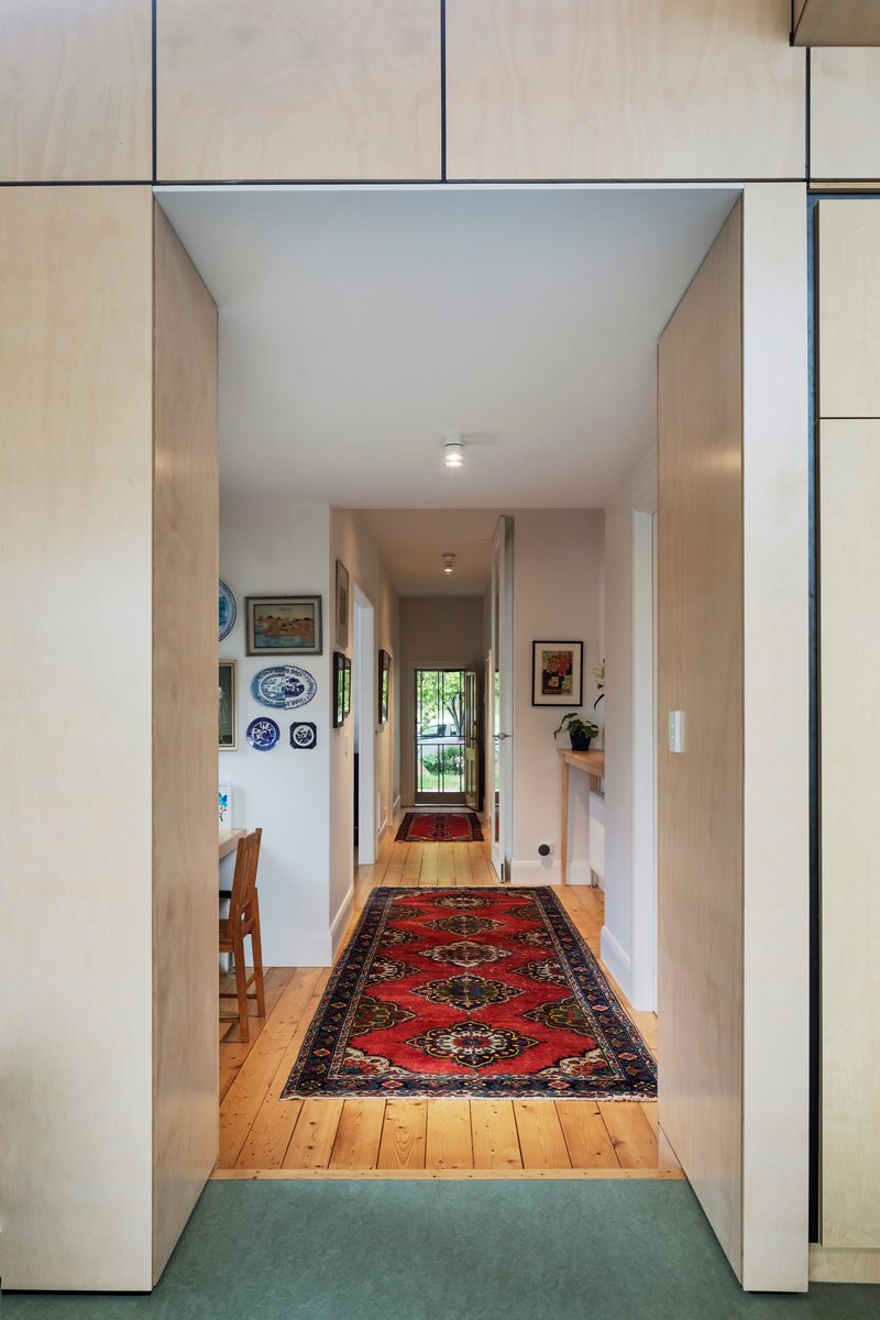 This architectural photo showcases a long hallway with a red oriental rug running down the center. The walls are white with decorative plates and paintings, and