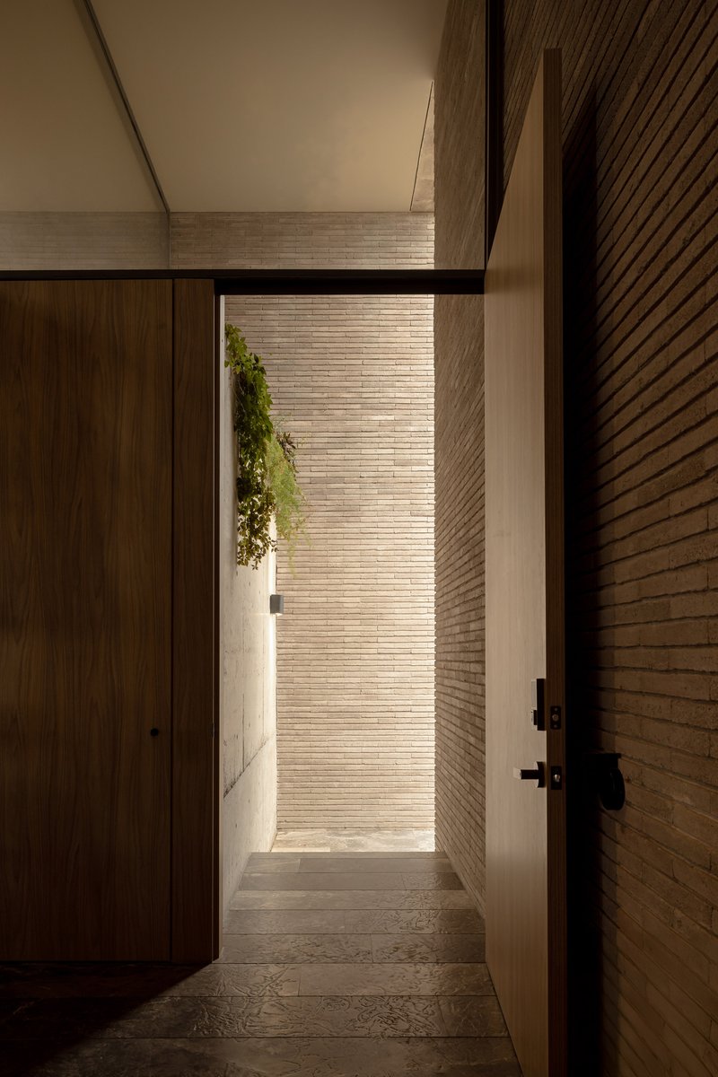 Entrance passage framing a courtyard with brick walls and hanging greenery in afternoon light