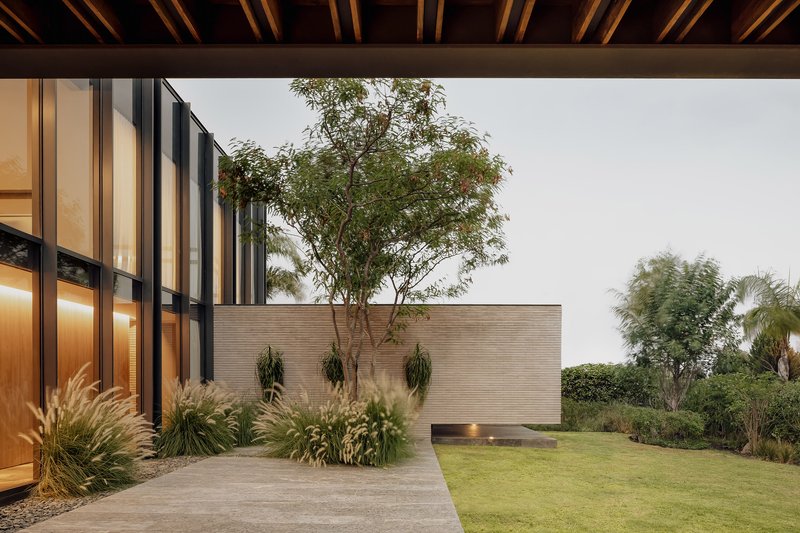 Garden view showing brick wall volumes with planted beds and a tree under overcast sky