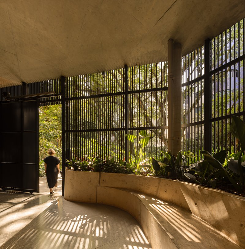 Lobby space with vertical brise-soleil casting striped shadows across curved concrete planter and stone floor