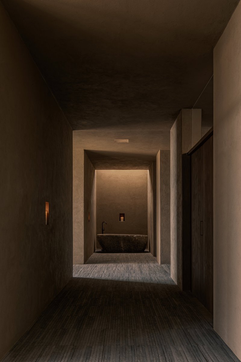Layered concrete threshold spaces framing a stone basin under concealed ceiling lighting