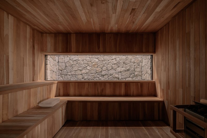 Timber-lined sauna interior with horizontal stone window panel and tiered bench seating