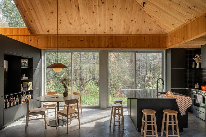 Open kitchen and dining area with knotty pine ceiling and full-height glazing overlooking forest