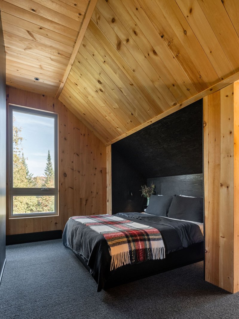 Bedroom with vaulted knotted pine ceiling and corner window framing evergreen forest views