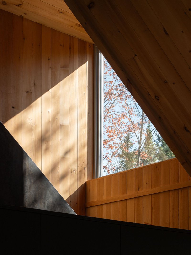 Triangular window cut through timber wall panels with sunlight casting diagonal shadows