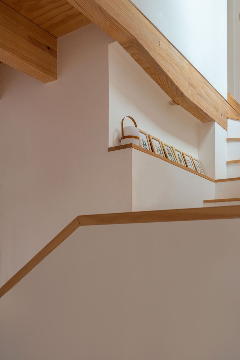 Interior staircase with timber treads and handrail ascending beneath exposed timber ceiling joists and white plaster walls
