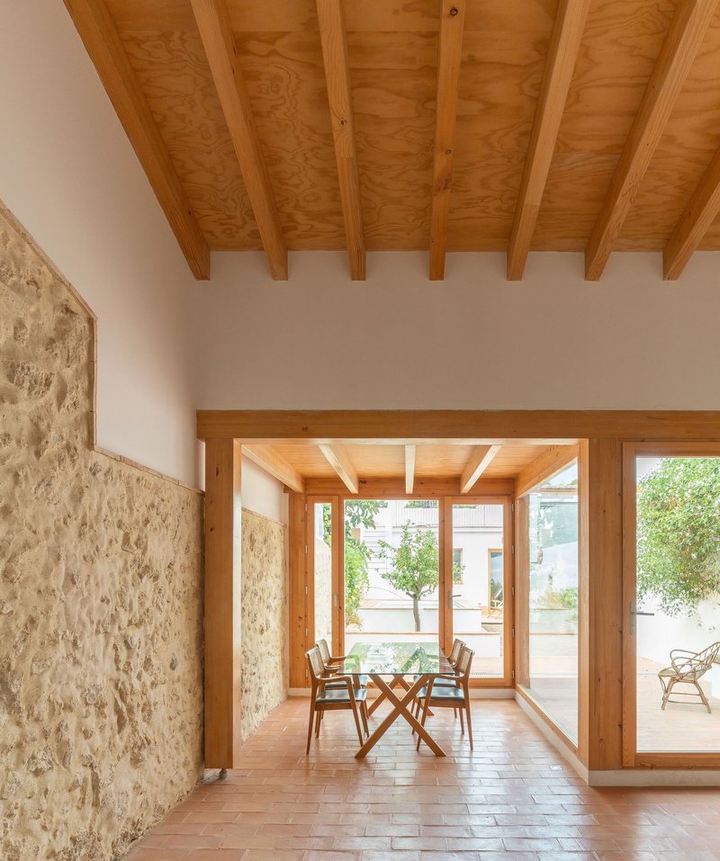 Interior dining space with exposed timber ceiling beams and stone wall opening onto terracotta tile patio