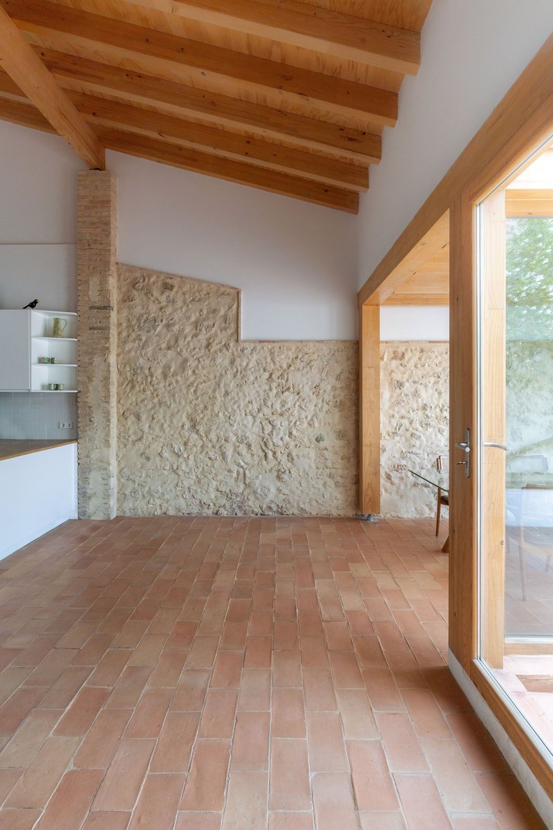 Interior room with terracotta tile floor and rough stone wall beneath exposed timber beam ceiling