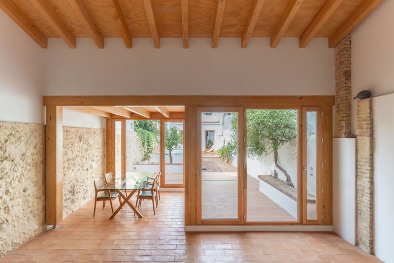 Interior room with exposed timber beams and terracotta floor opening to a courtyard through timber-framed glass doors