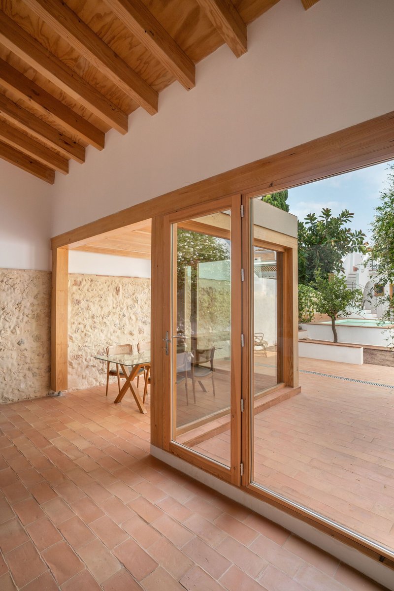 Interior view through timber-framed glass doors opening to a courtyard with stone wall under blue sky