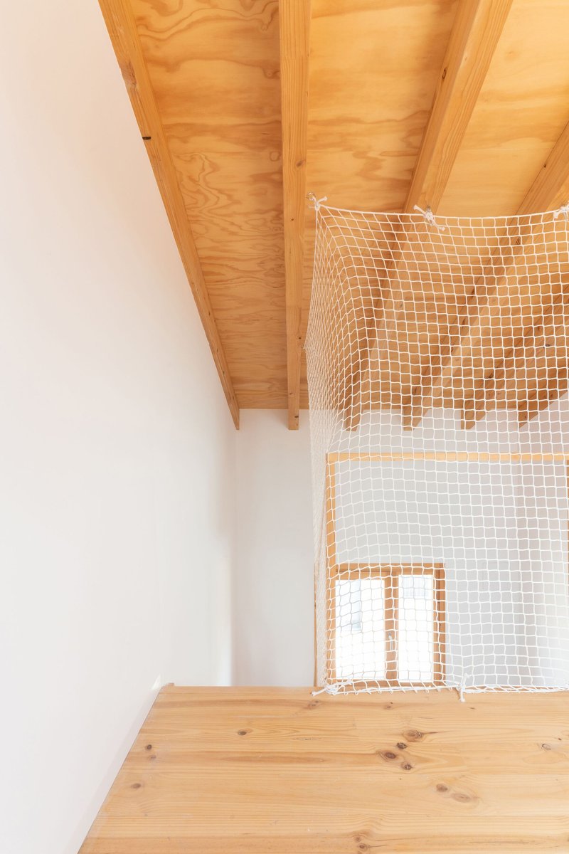 Looking up at rope mesh safety net stretched between timber ceiling planes across a double-height space
