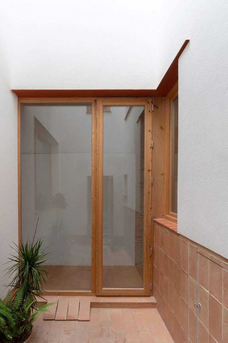 Small courtyard with timber-framed glass doors, terracotta paving and single potted plant in corner
