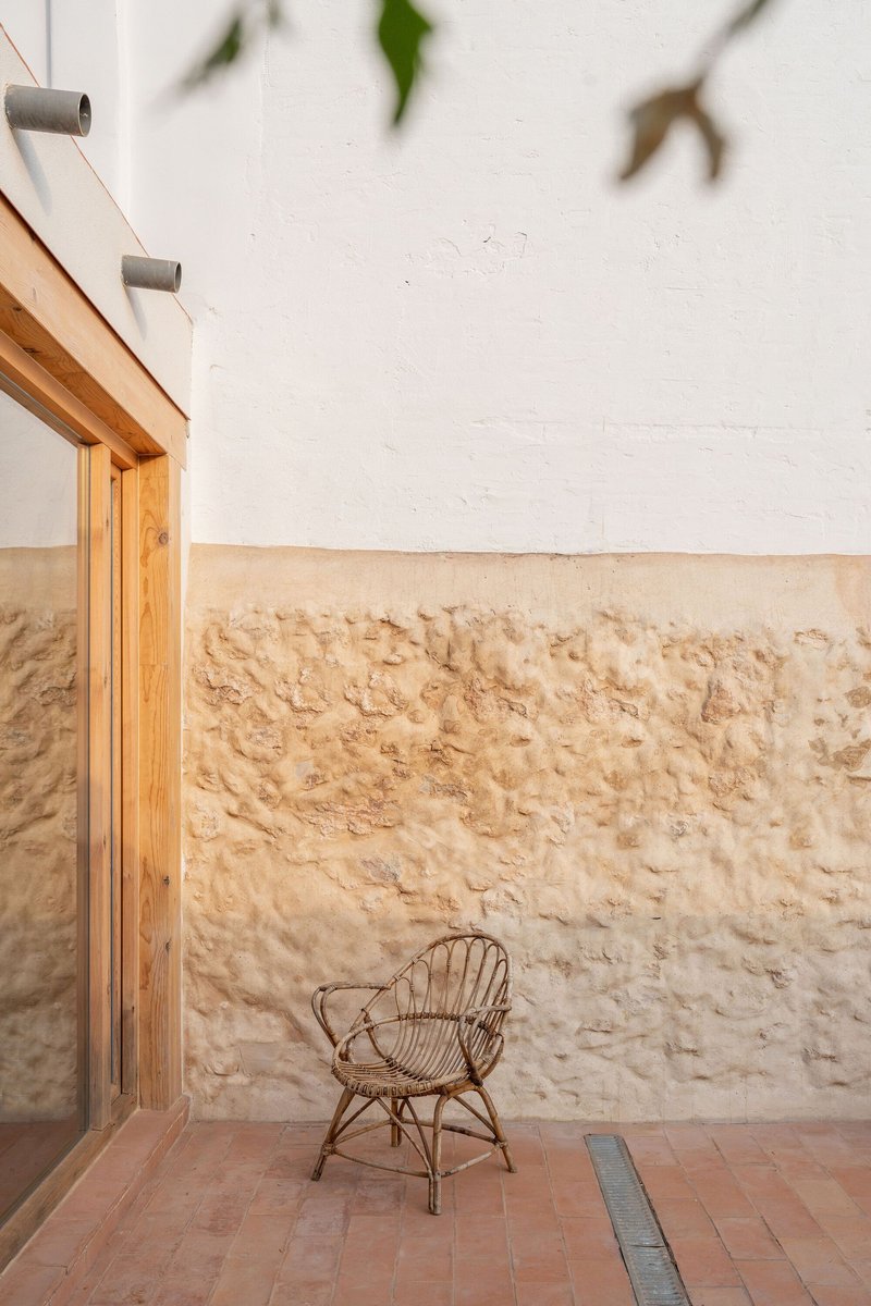 Interior courtyard with rough limestone wall, terracotta tile floor and a wicker chair beneath dappled shade