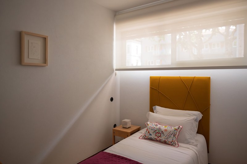 Bedroom with yellow upholstered headboard beneath a high window with translucent roller shade
