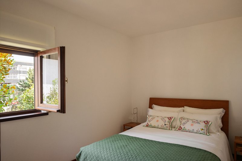 Bedroom with wood-framed window overlooking neighboring buildings and greenery