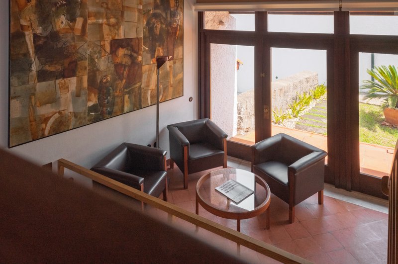 Living area with leather armchairs and patchwork stone wall overlooking a coastal landscape through dark timber doors