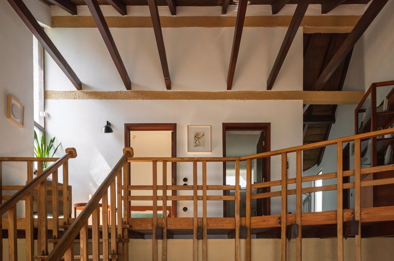 Timber railings around an upper level balcony with exposed ceiling beams and white plaster walls