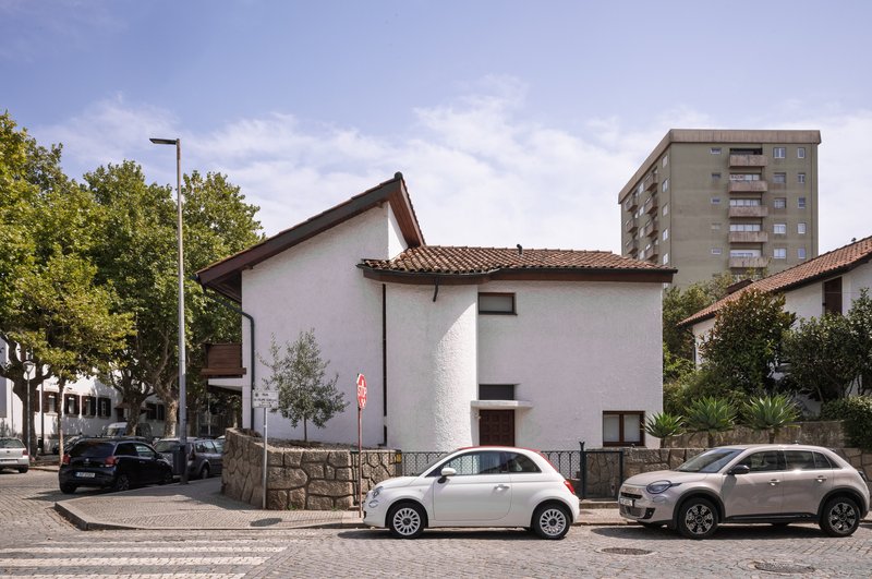 Street view of the white stucco house with terracotta tile roof between parked cars