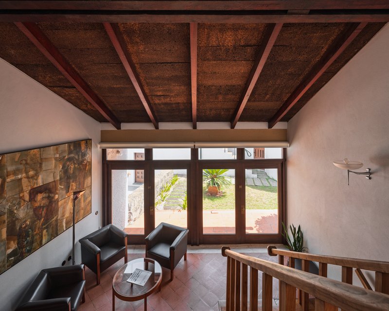 Upper-level sitting area with exposed timber beams and cork ceiling panels overlooking the garden