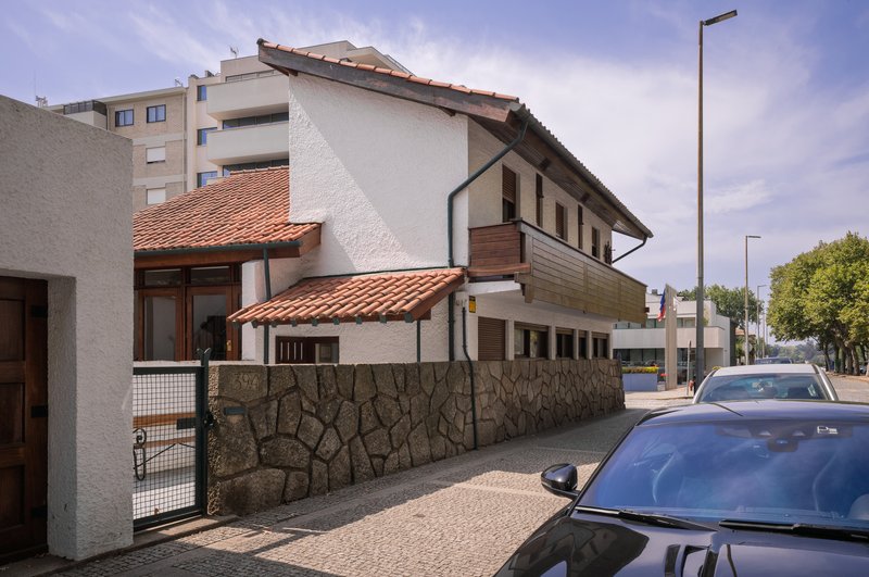 Street view of the white residence with terracotta tile roofs above a rusticated stone base wall