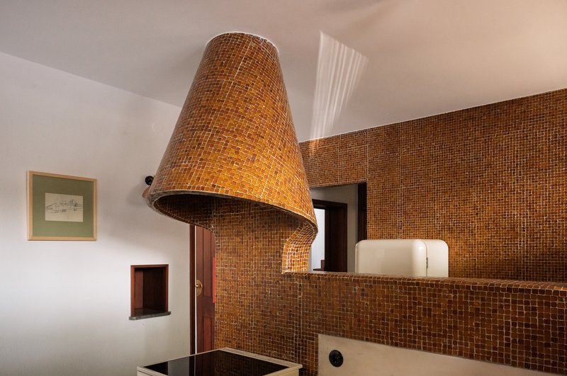 Conical bronze mosaic tile range hood above the cooktop with skylight overhead