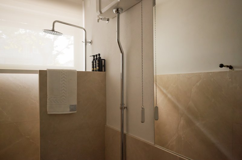 Shower enclosure with beige stone panels and exposed plumbing with chain-pull controls