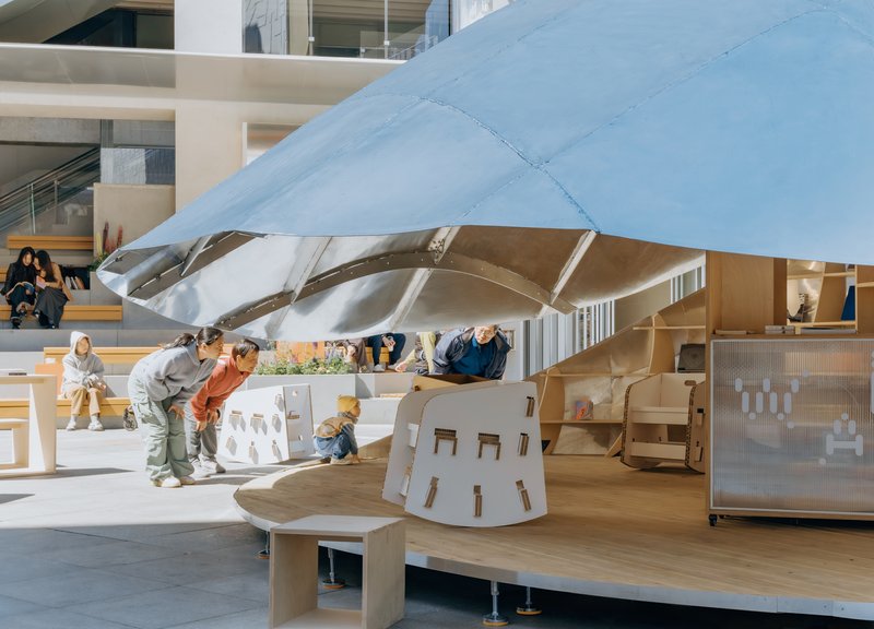 White shell canopy supported by exposed metal ribs above a timber play deck with children and families
