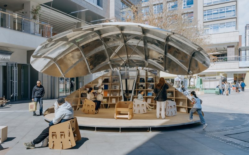 Side view of the circular pavilion showing the dome's structural frame and plywood base with visitors seated