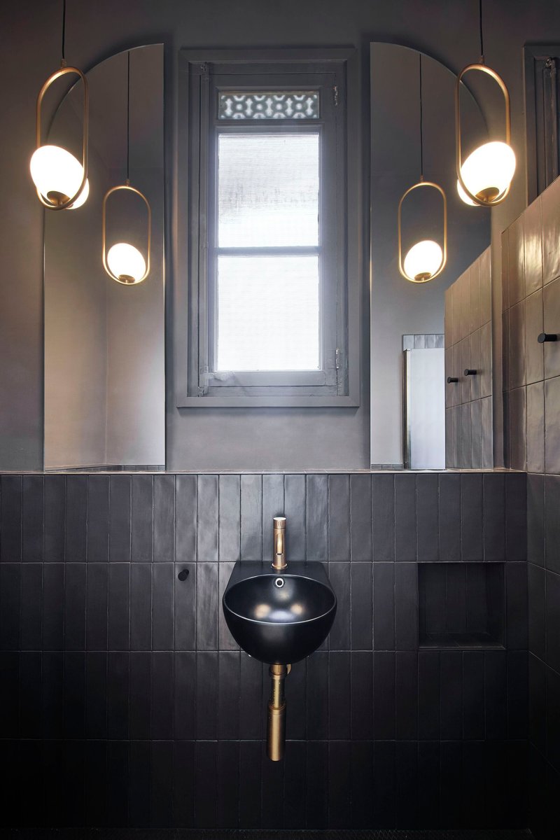 Bathroom vanity with black bowl sink, dark vertical tiles, and paired brass pendant lights