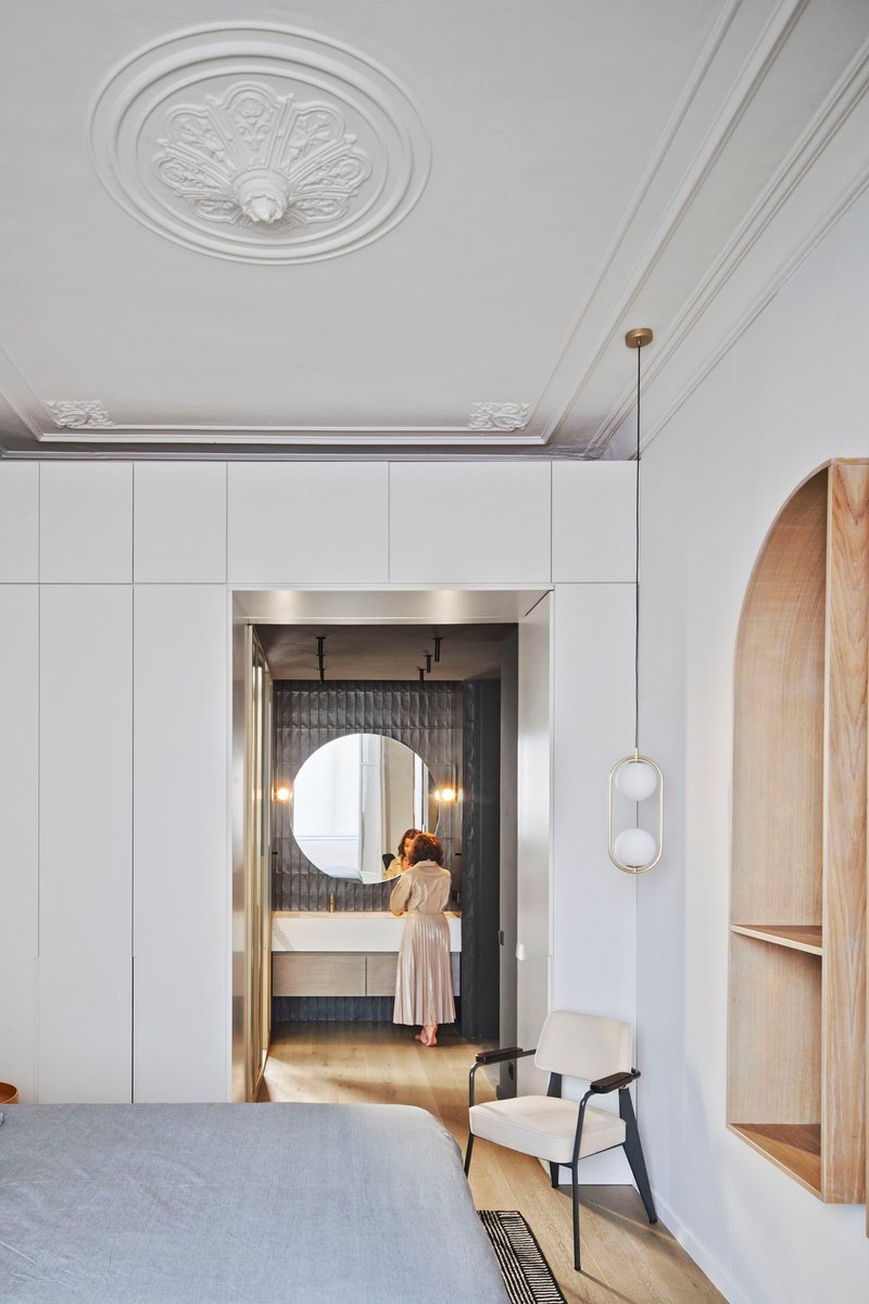 Bedroom with ornamental ceiling medallion and view through doorway to ensuite bathroom where figure stands at vanity