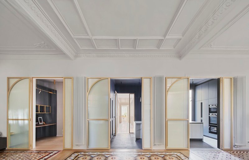 Three brass-framed glass doors with arched tops open from a coffered ceiling room to adjacent spaces