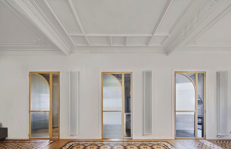 Three brass-framed arched doorways with vertical radiators between them beneath a coffered ceiling