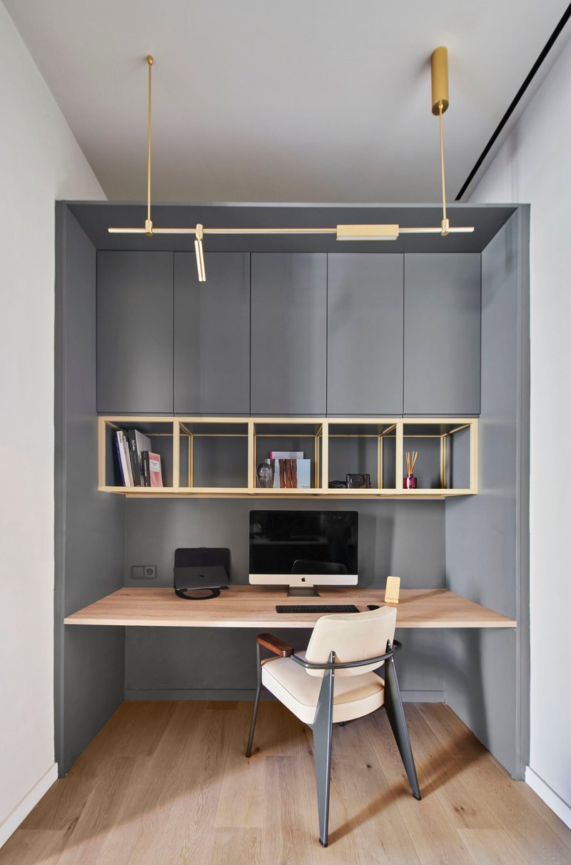 Built-in workspace alcove with grey cabinetry, timber desk, and brass-framed open shelving above