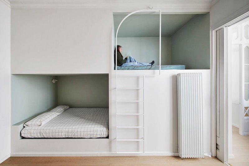 White bunk bed unit with arched upper alcove and ladder access with person reading on top bunk