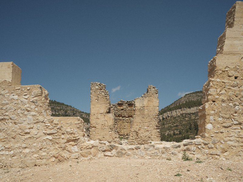 Interior view of ruined stone walls with exposed masonry against a clear blue sky and distant hills