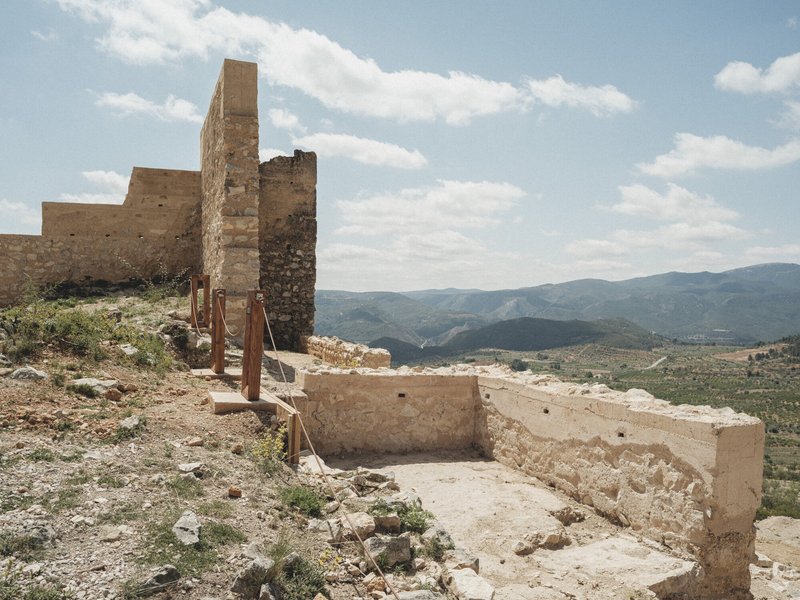 Stone parapet edge with wooden safety barrier overlooking rolling hills and valleys beyond