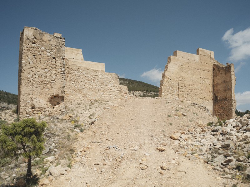 Stepped rammed earth walls flanking a gravel path ascending a hillside under clear blue sky
