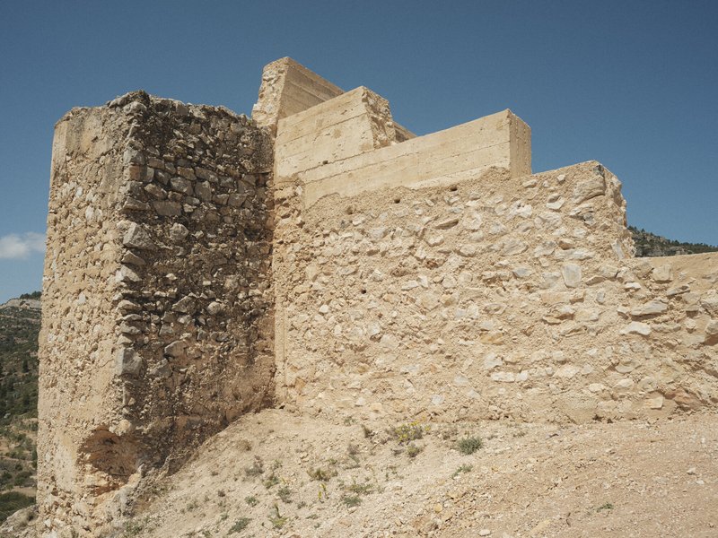 Weathered stone fortification walls with cylindrical tower rising against a clear blue sky