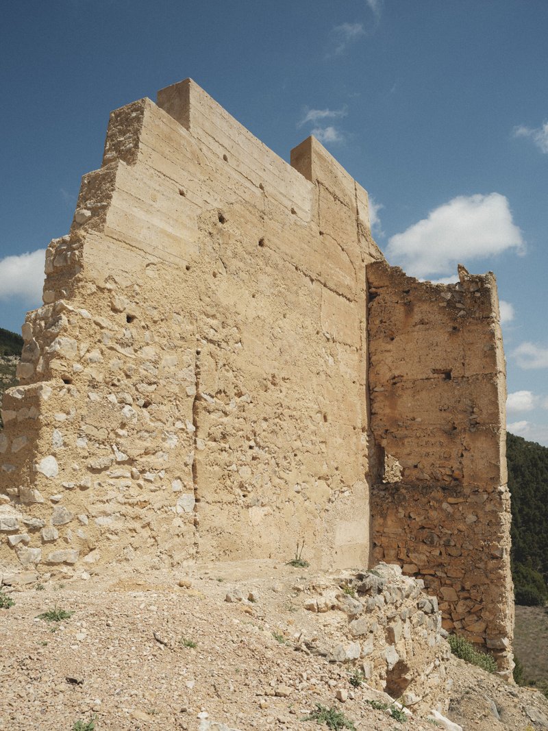 Stepped rammed earth wall with embedded timber formwork holes under scattered clouds