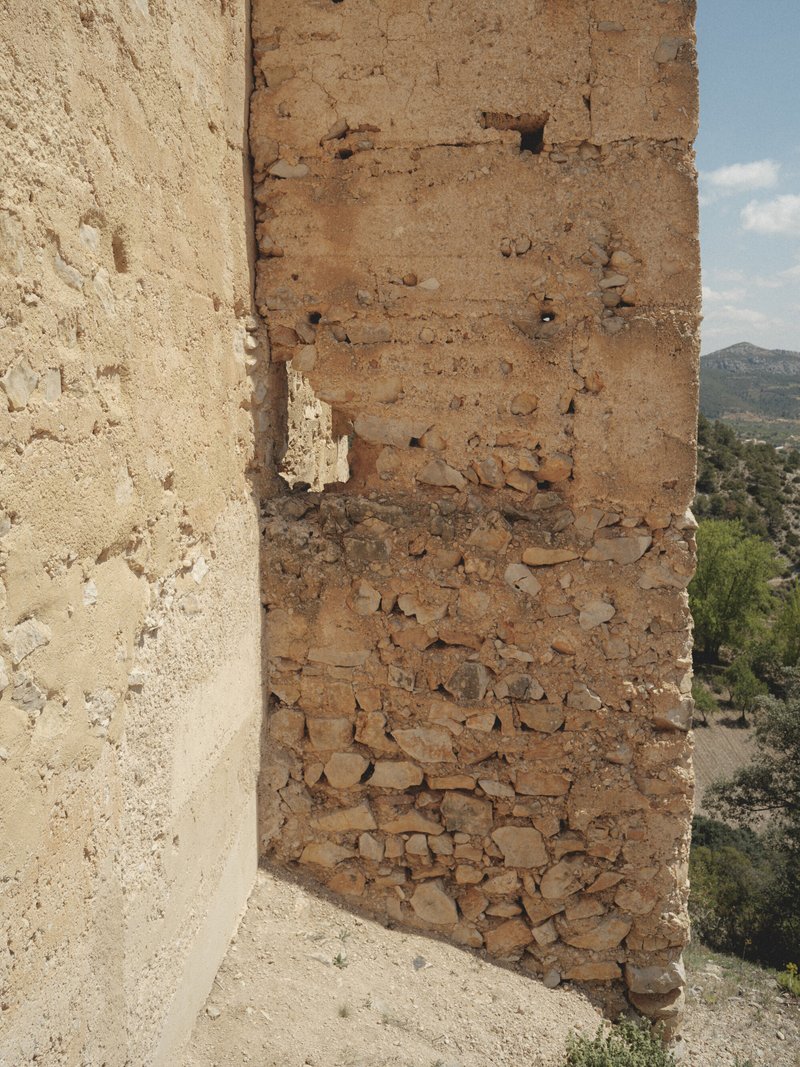 Close-up of layered rammed earth wall section showing horizontal construction lines and erosion