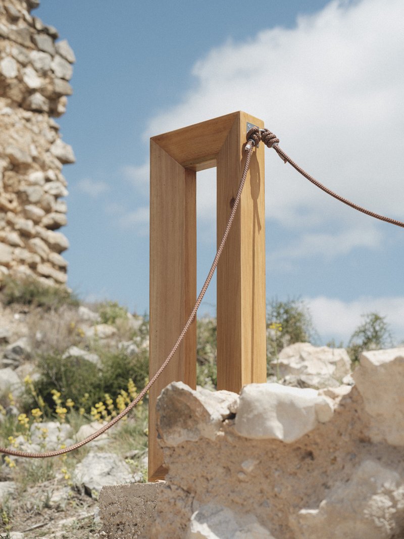 Timber portal frame with rope barrier standing among ancient stone ruins under midday sun