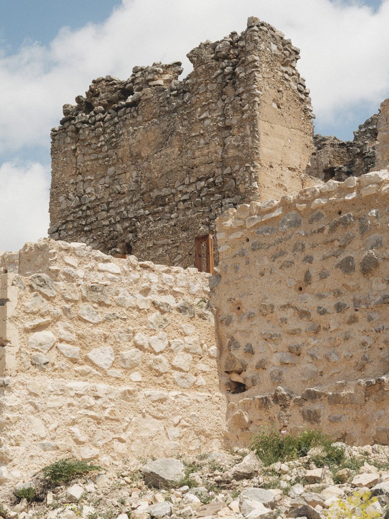 Crumbling stone walls with a small wooden door opening under a partly cloudy sky